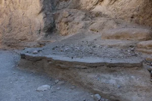 A knee-high slab of pavement rests on a rock slab while tan canyon walls tower behind.
