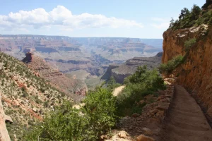A dirt trail with steps descends into the canyon past a short cliff of white limestone.