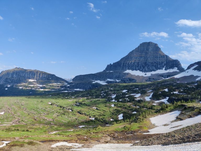 Expansive view of mountains and valleys in Glacier National Park with clear blue skies.