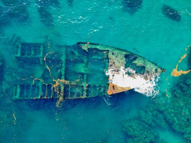 A stunning aerial view of a rusty sunken shipwreck submerged in clear turquoise waters.