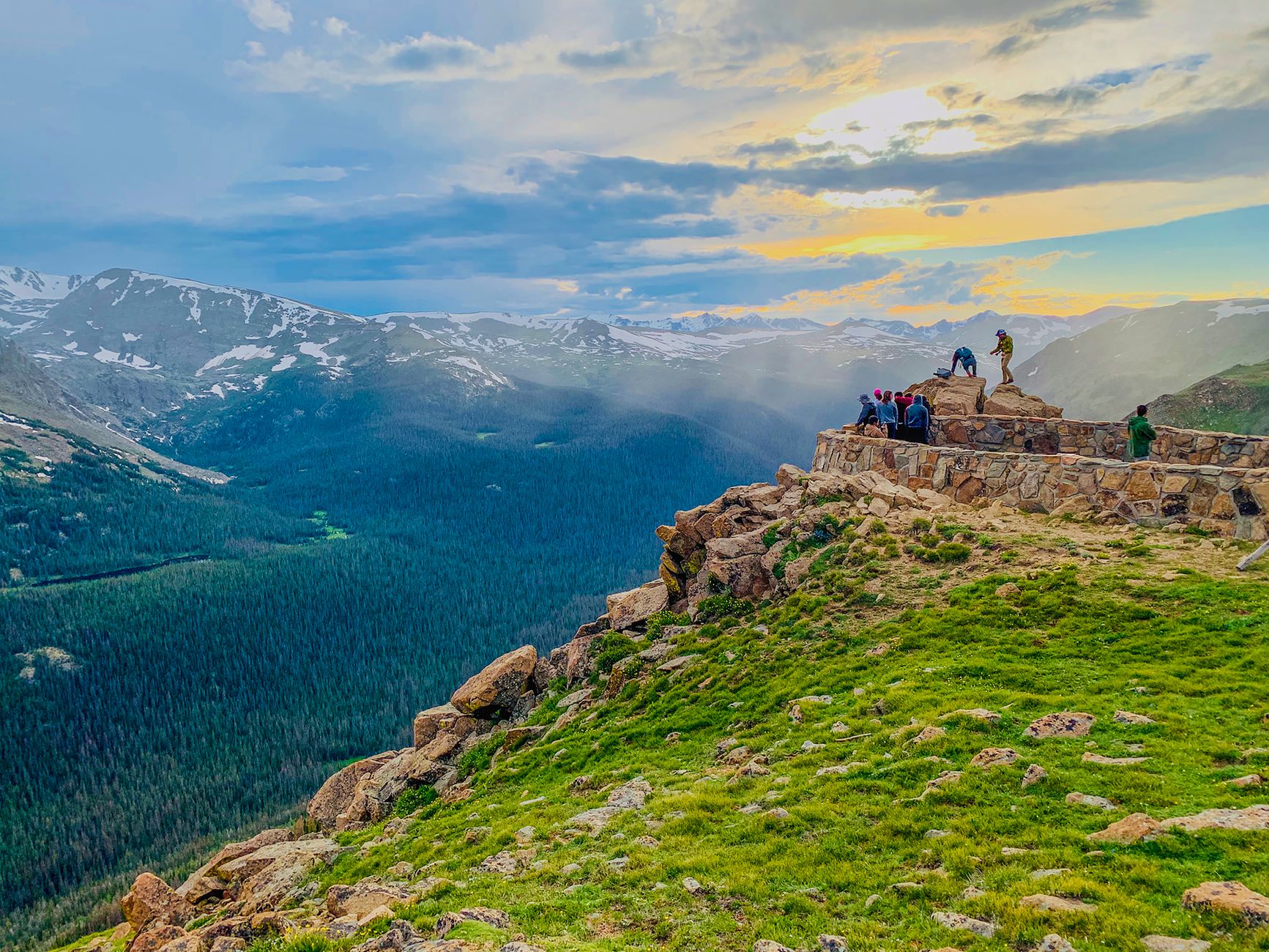 Anonymous travelers standing on stony observation point in Forest Canyon of Rocky Mountain National Park and admiring breathtaking view during sunset in Colorado
