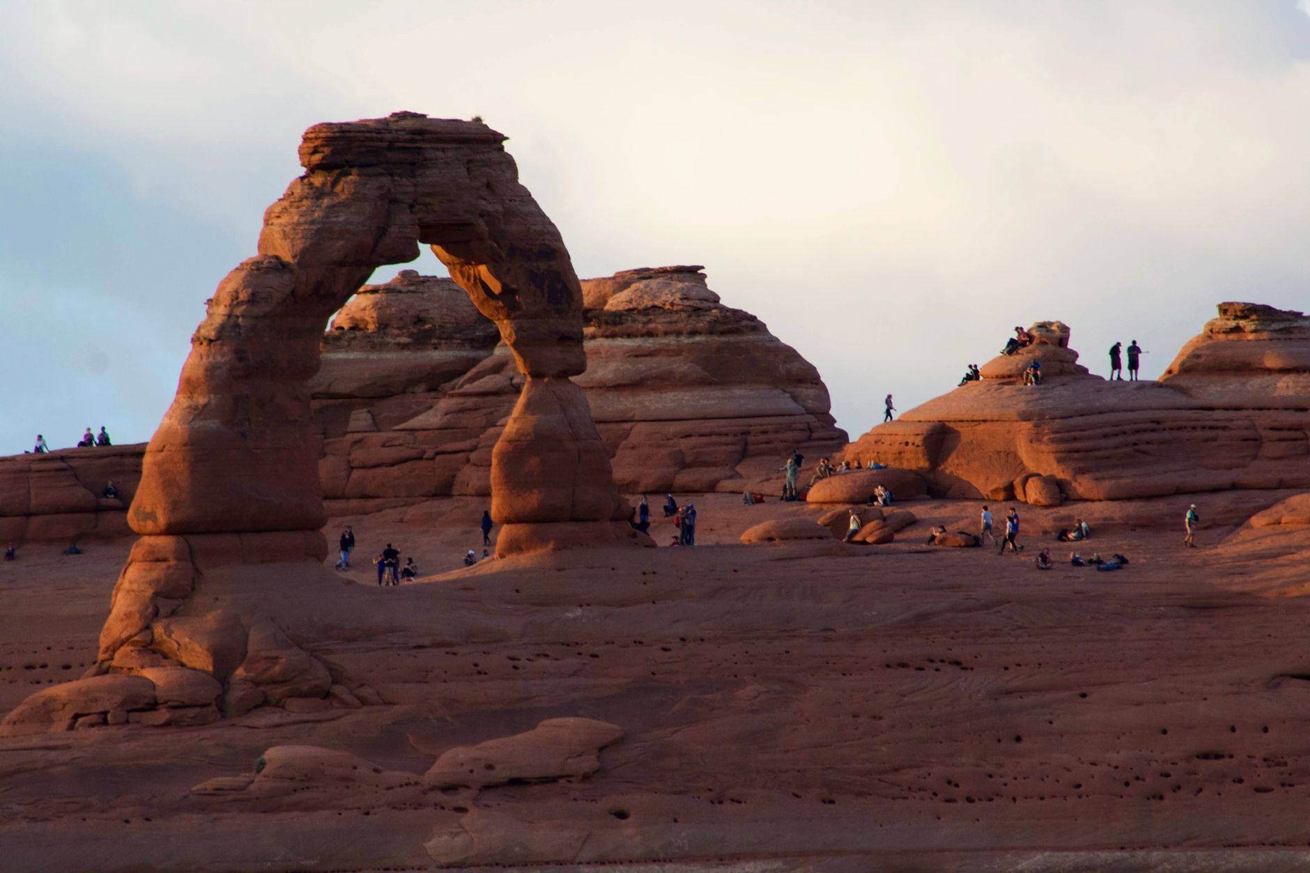 Tourists explore the iconic Delicate Arch at sunset in Arches National Park, Utah.