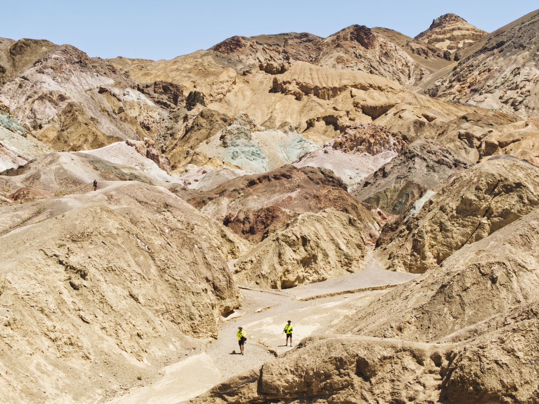 Two hikers explore the vibrant, mineral-rich hills of Death Valley's arid terrain.