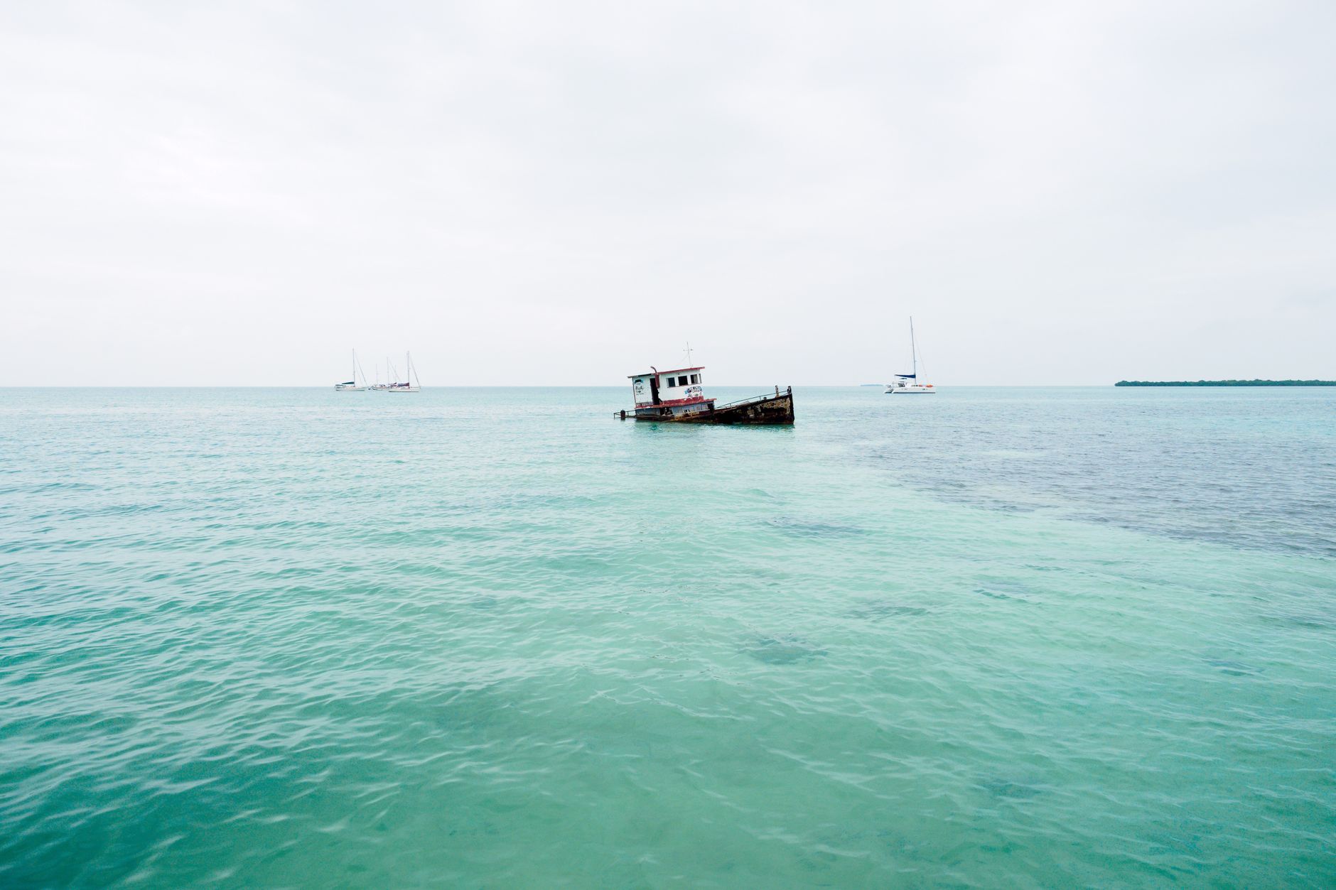 A peaceful seascape featuring an old shipwreck and yachts against a serene horizon.