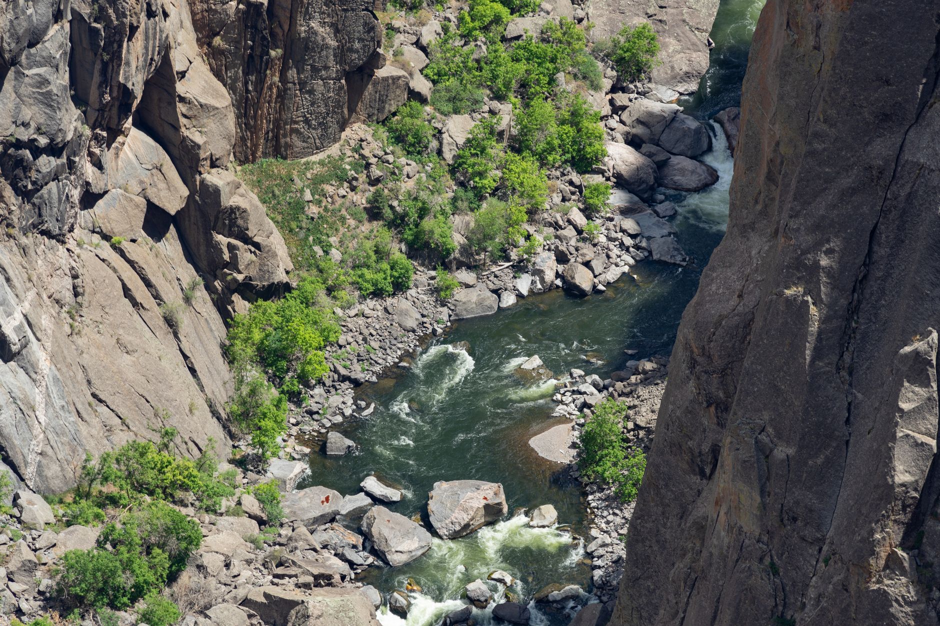 Aerial view of a vibrant stream flowing through rocky canyon walls in Gunnison, showcasing summer greenery.