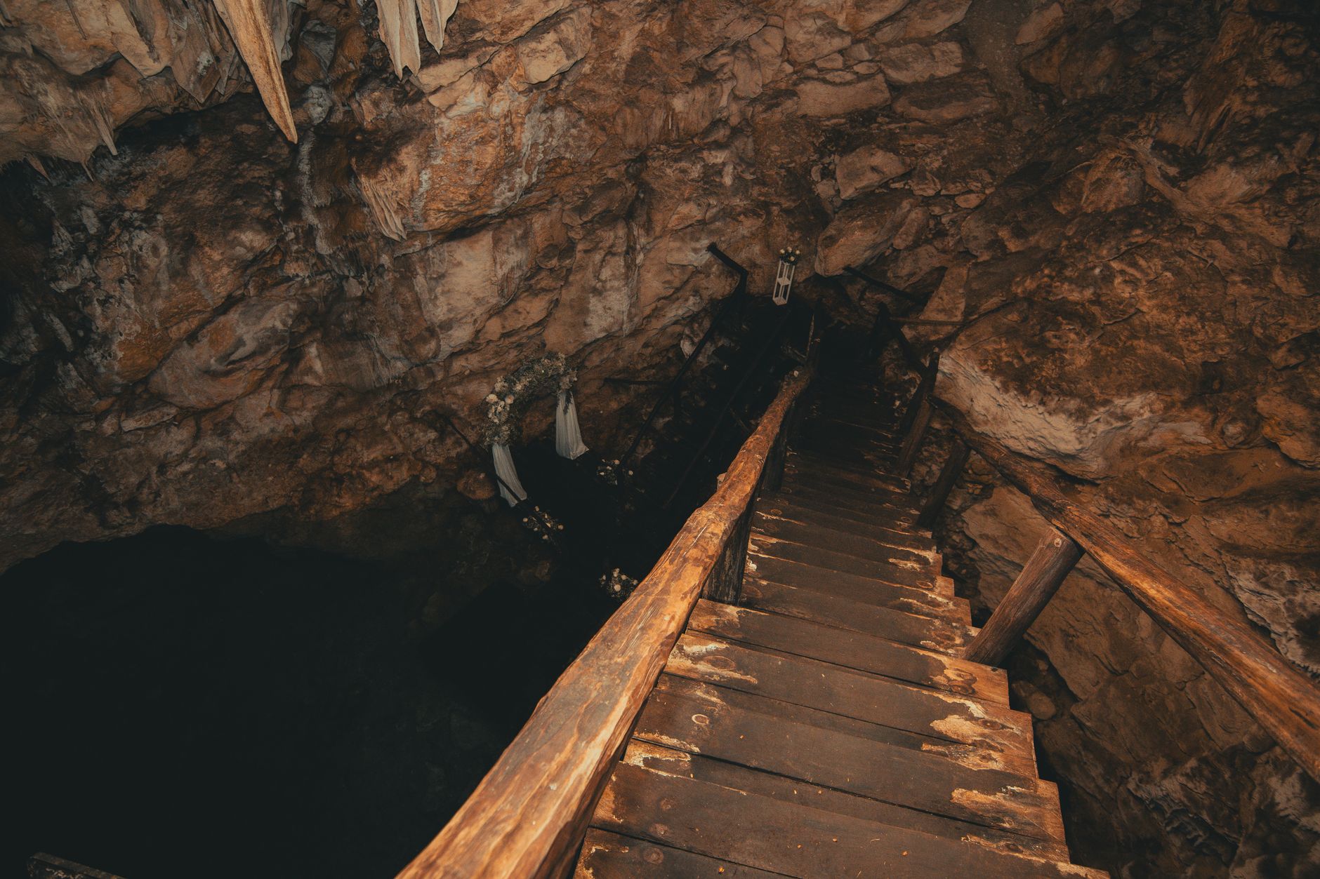 Explore the rugged beauty of a cave with rustic wooden stairs and stalactites.