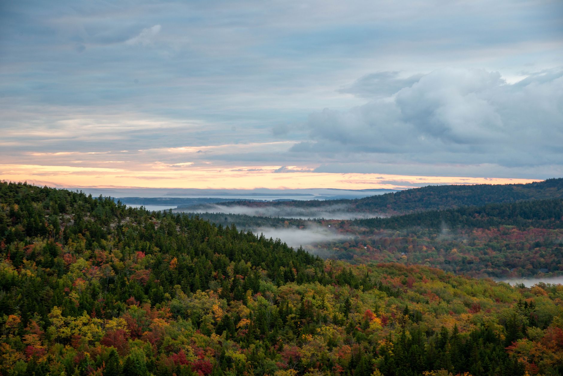 Stunning view over Acadia National Park's autumn foliage with misty sunrise.