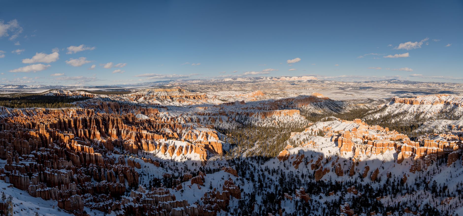 Stunning panoramic view of Bryce Canyon in winter with snow-covered hoodoos and clear blue skies.