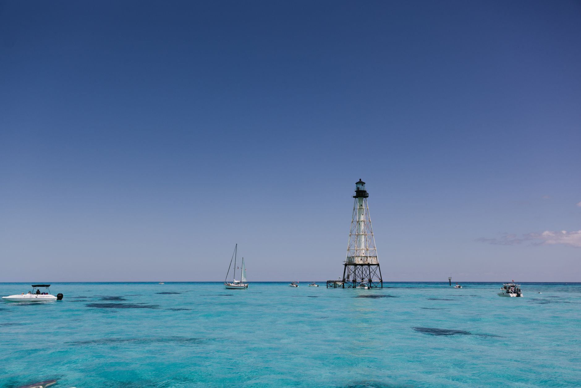 Tranquil scene featuring a lighthouse surrounded by clear turquoise waters with a few boats.