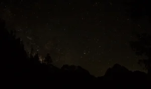 A starry night sky above a ridge of rocky mountain peaks.