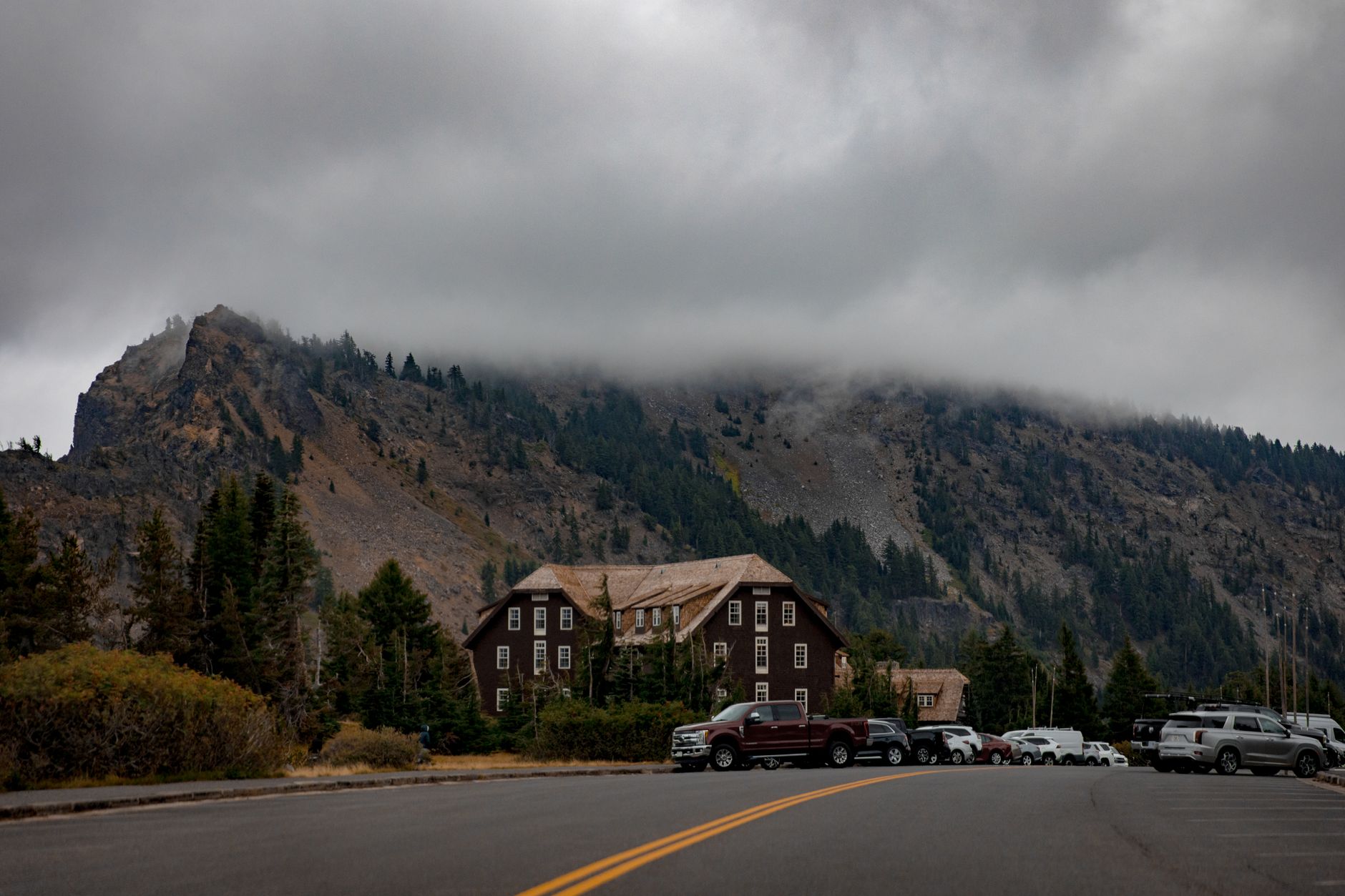 Fog envelops Crater Lake Lodge in Oregon, surrounded by trees and mountains.