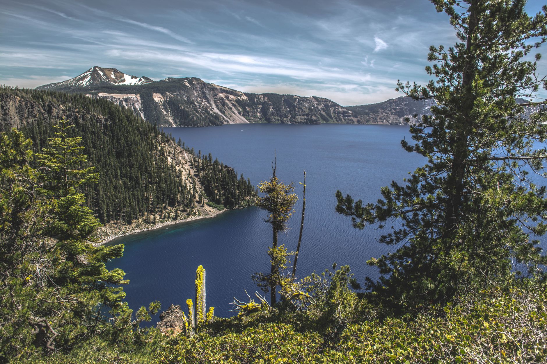 Breathtaking view of Crater Lake surrounded by mountains and evergreen trees under a clear sky.