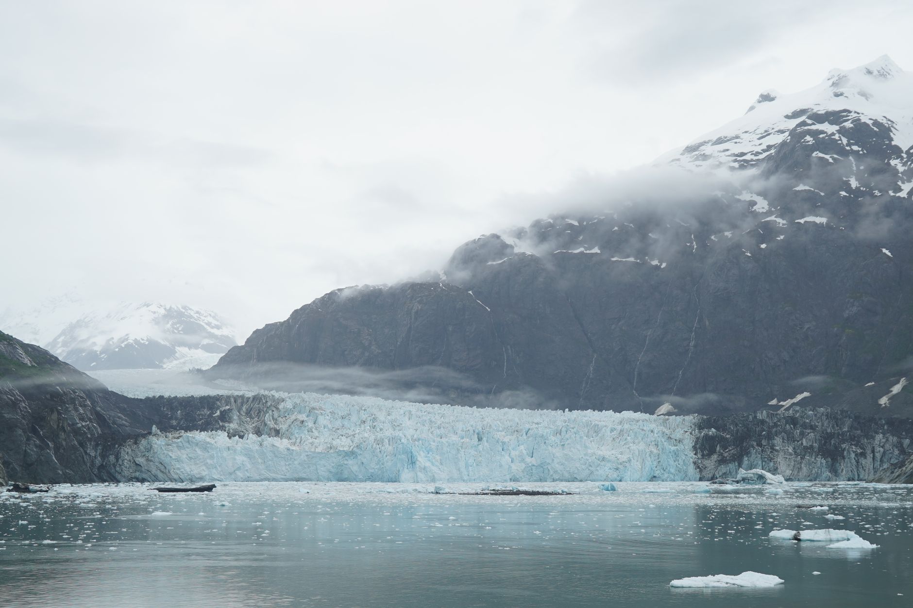 Panoramic view of a glacier with surrounding snow-capped mountains and misty clouds.