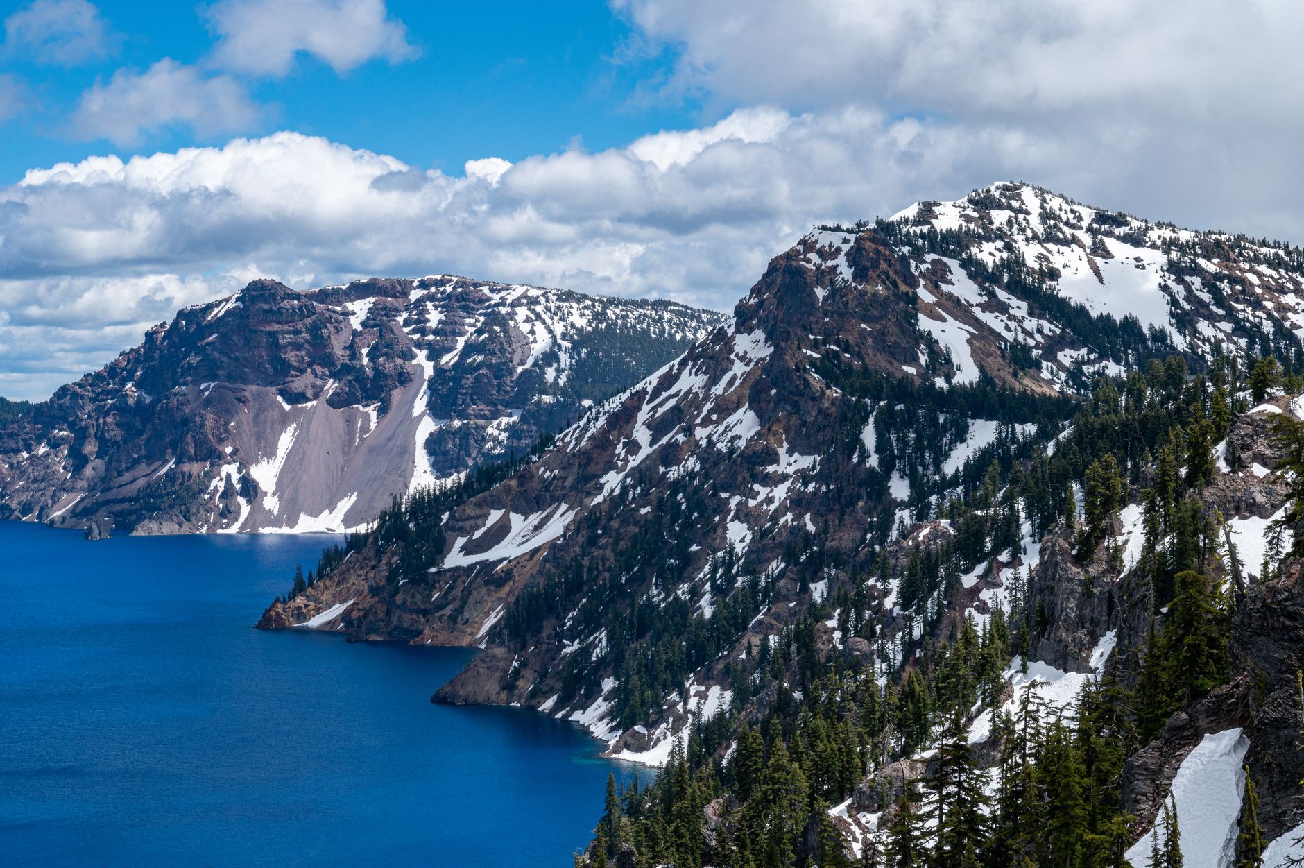 Stunning snow-capped mountains overlooking Crater Lake under a blue sky, capturing nature's beauty.