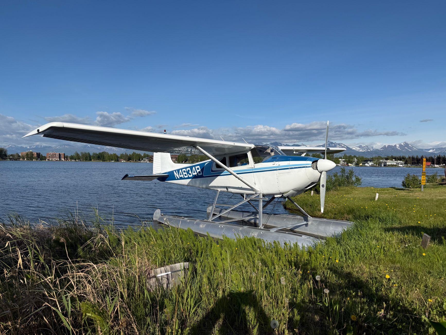 A scenic view of a seaplane docked by a lake, framed by distant mountains under a blue sky.