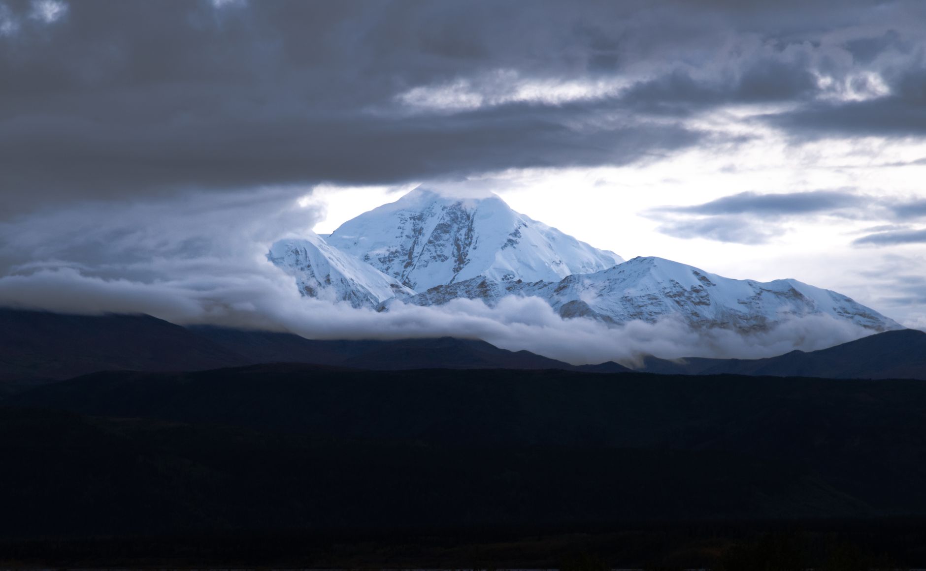 A stunning view of Denali Peak with clouds parting to reveal its snowcapped summit in Alaska.
