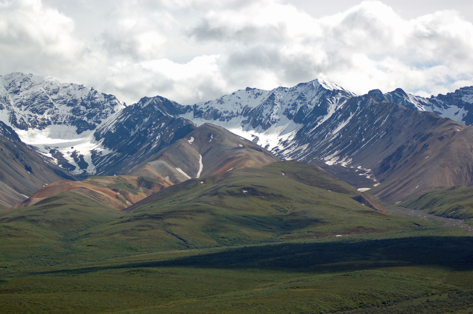 Breathtaking view of snowcapped mountains and green valleys under a cloudy sky.