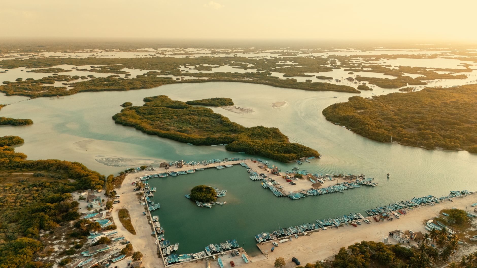 Aerial view of coastal wetlands with scattered islands and boats docked at sunset.