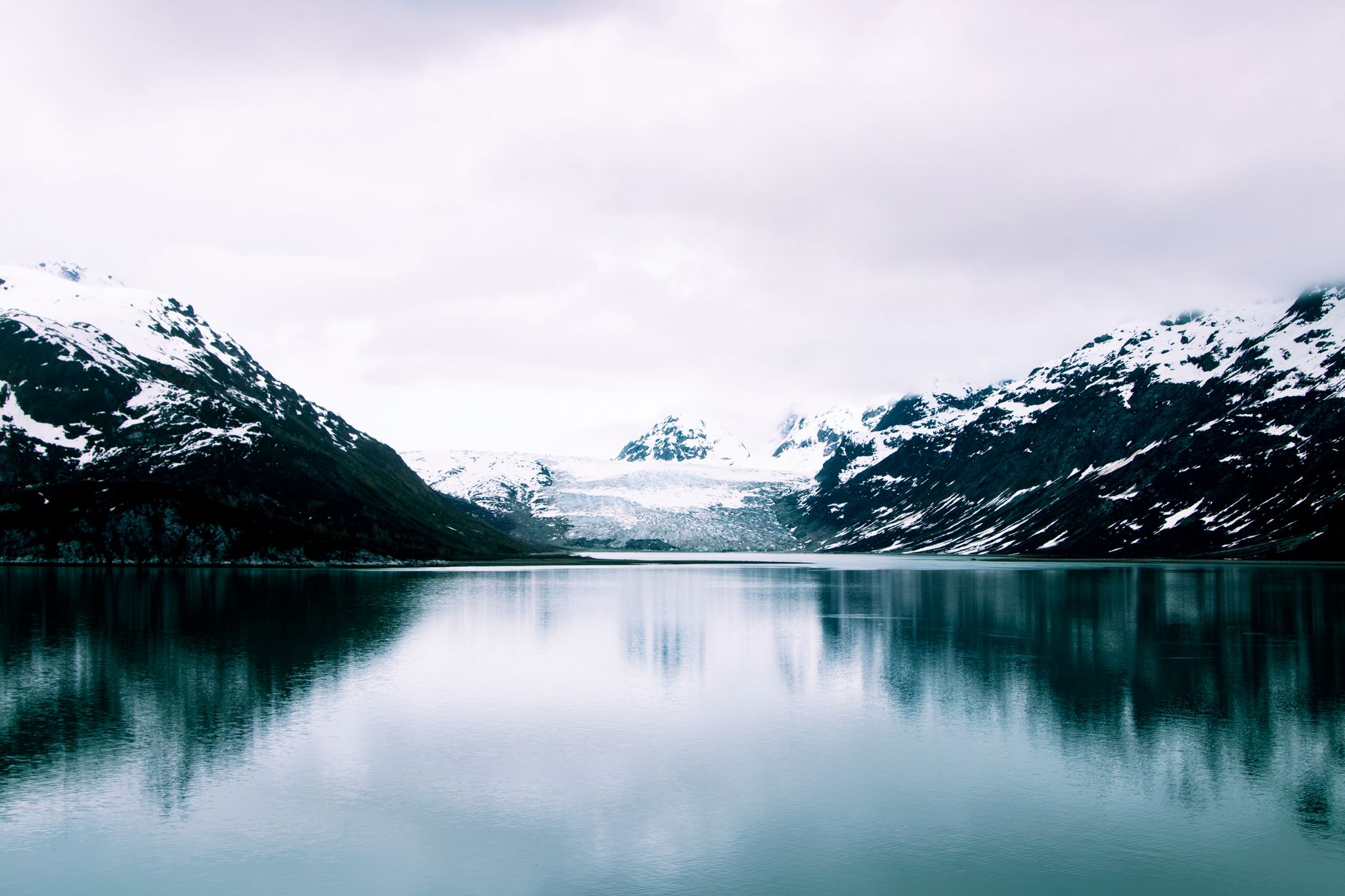 Stunning view of snowcapped mountains and calm lake in Alaska, showcasing serene natural beauty.
