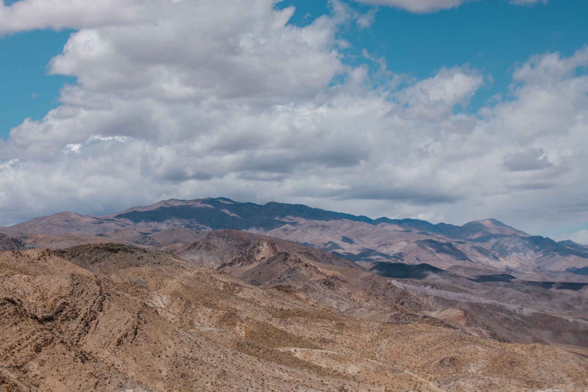 Breathtaking panorama of the arid Death Valley desert, showcasing rugged hills and a distant mountain range under vast clouds.