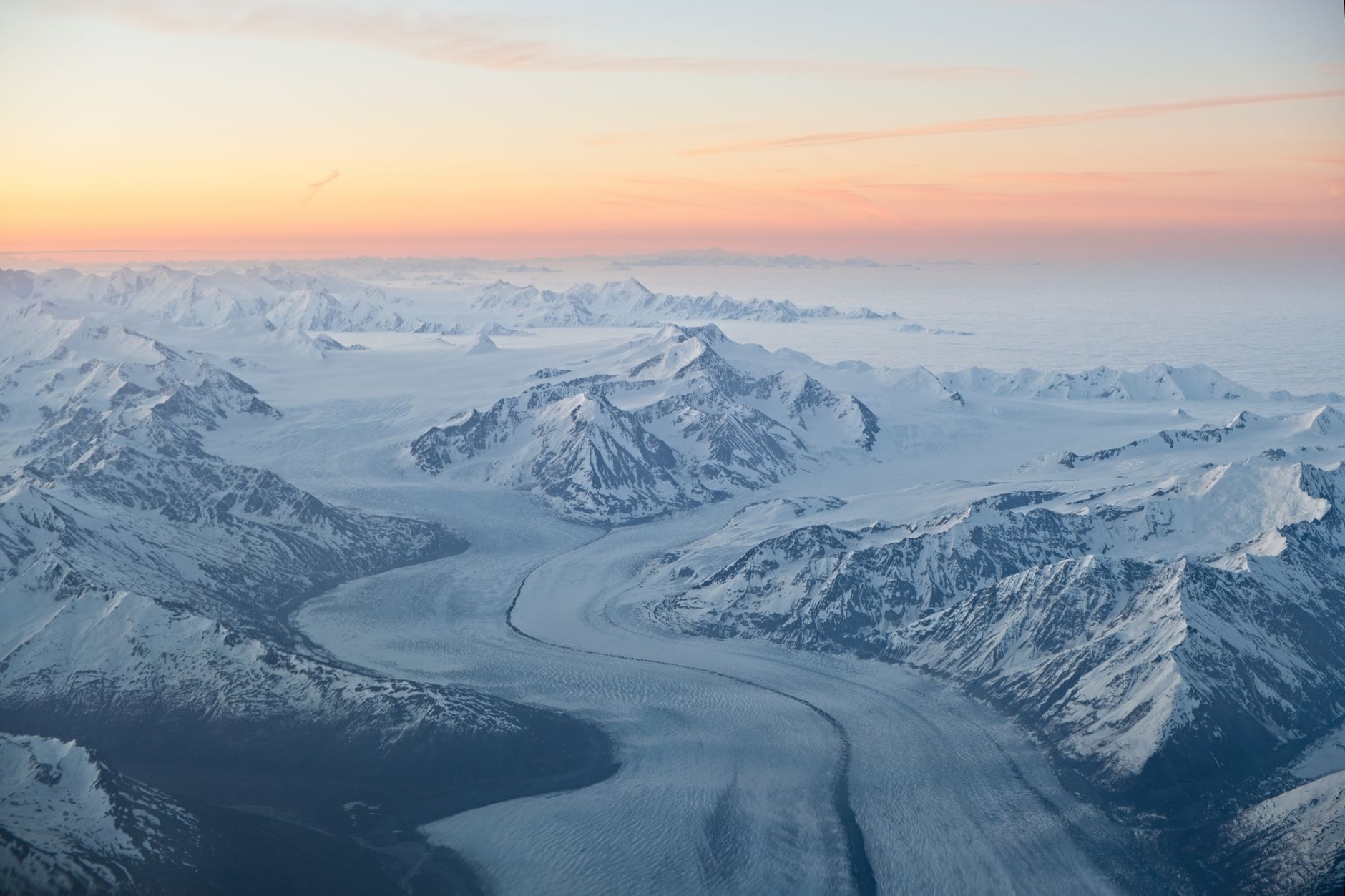 A breathtaking aerial view of the snow-covered mountains and glaciers in Alaska during sunset.