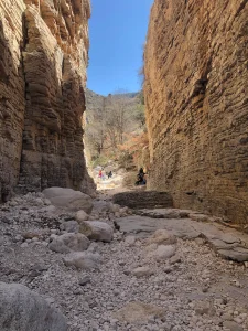 Groups of people in the sunlight at the end of a narrow tall canyon.