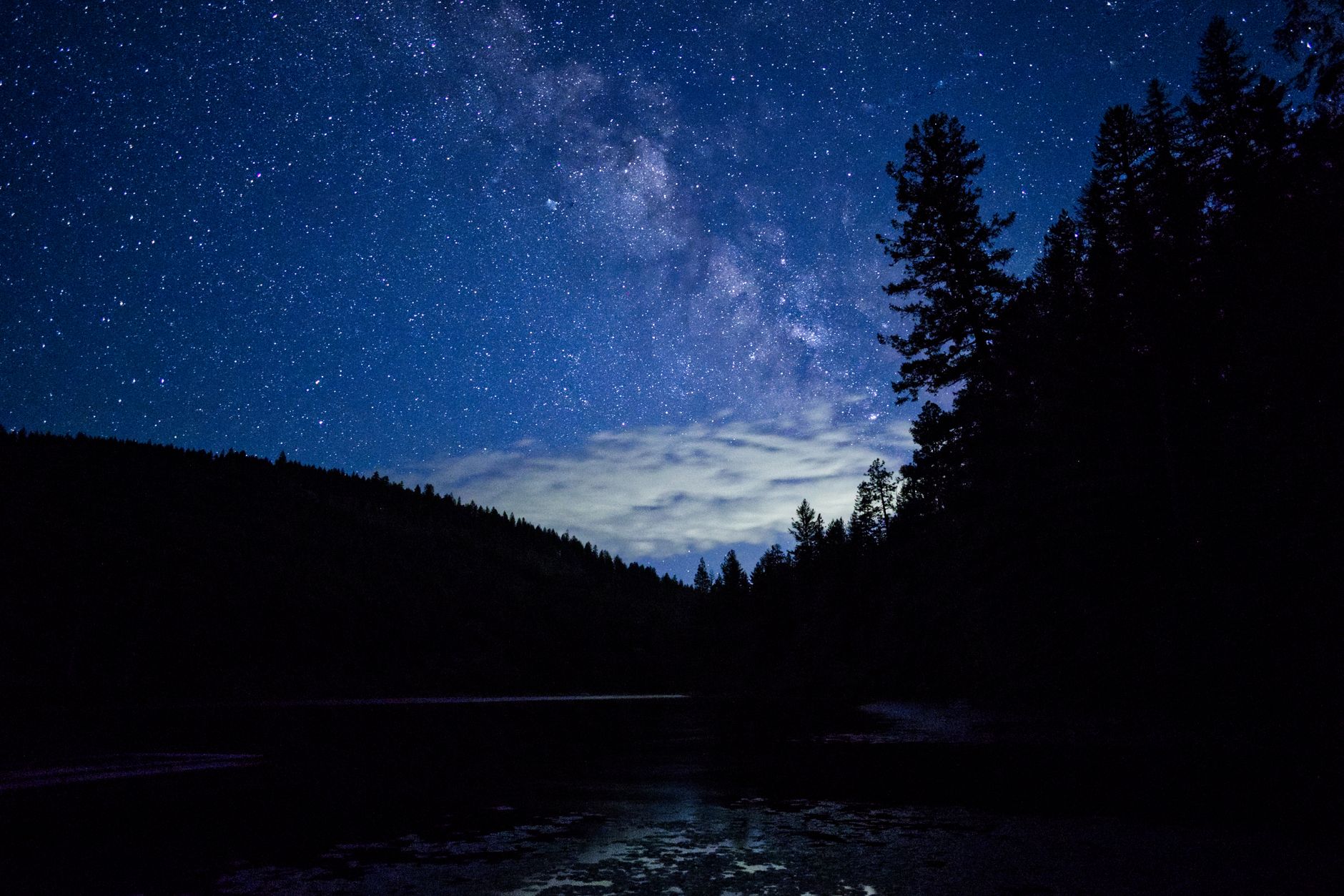 Stunning nightscape of the Milky Way galaxy over a serene lake and forest with clear reflection.