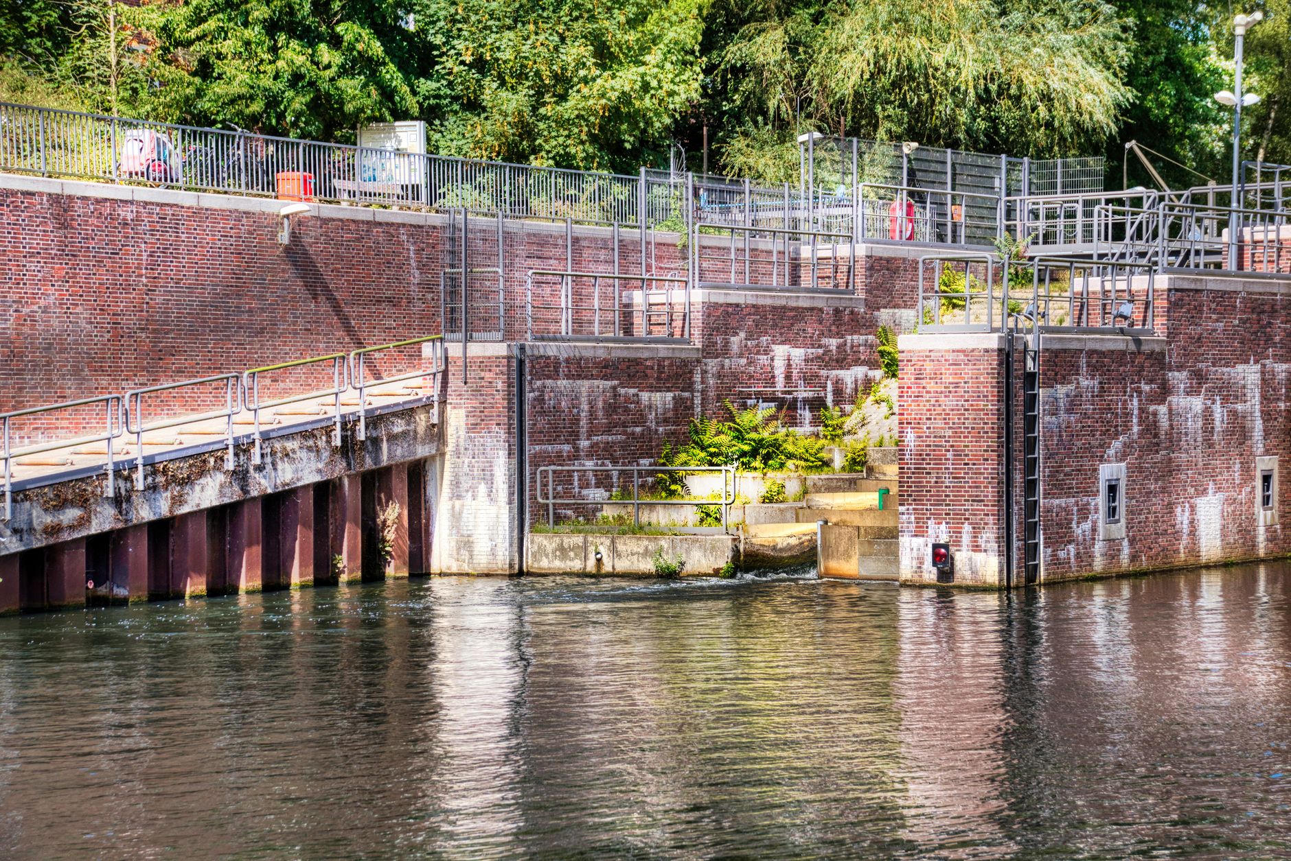 A brick canal lock by the water with lush greenery and railings, ideal for infrastructure themes.