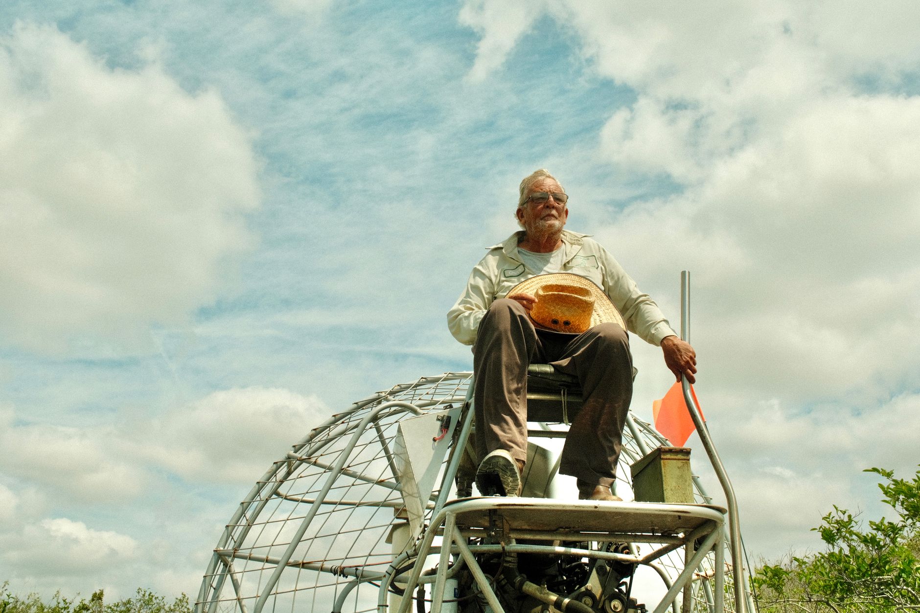 Elderly man navigating an airboat through the Florida Everglades on a sunny day.