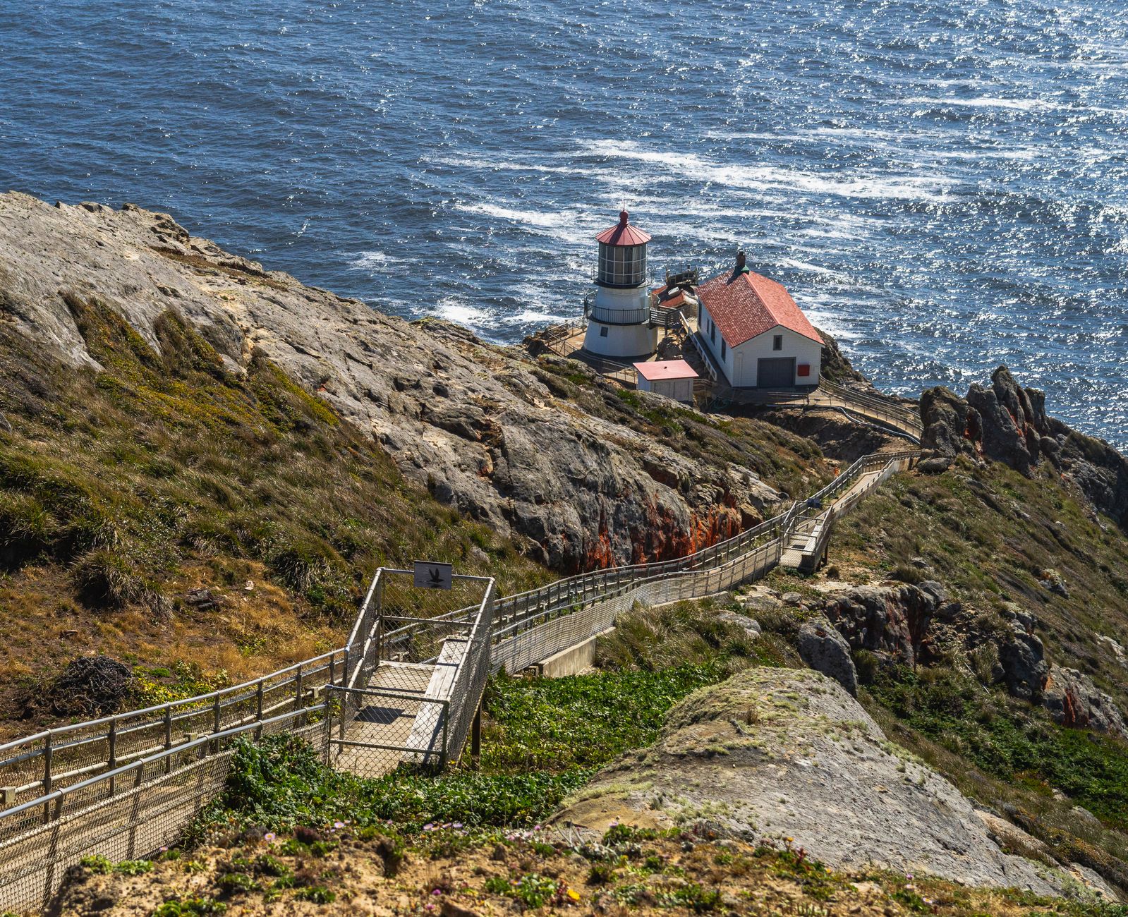 Captivating view of a lighthouse perched on a rocky coastline with a wooden path leading down to the sea.
