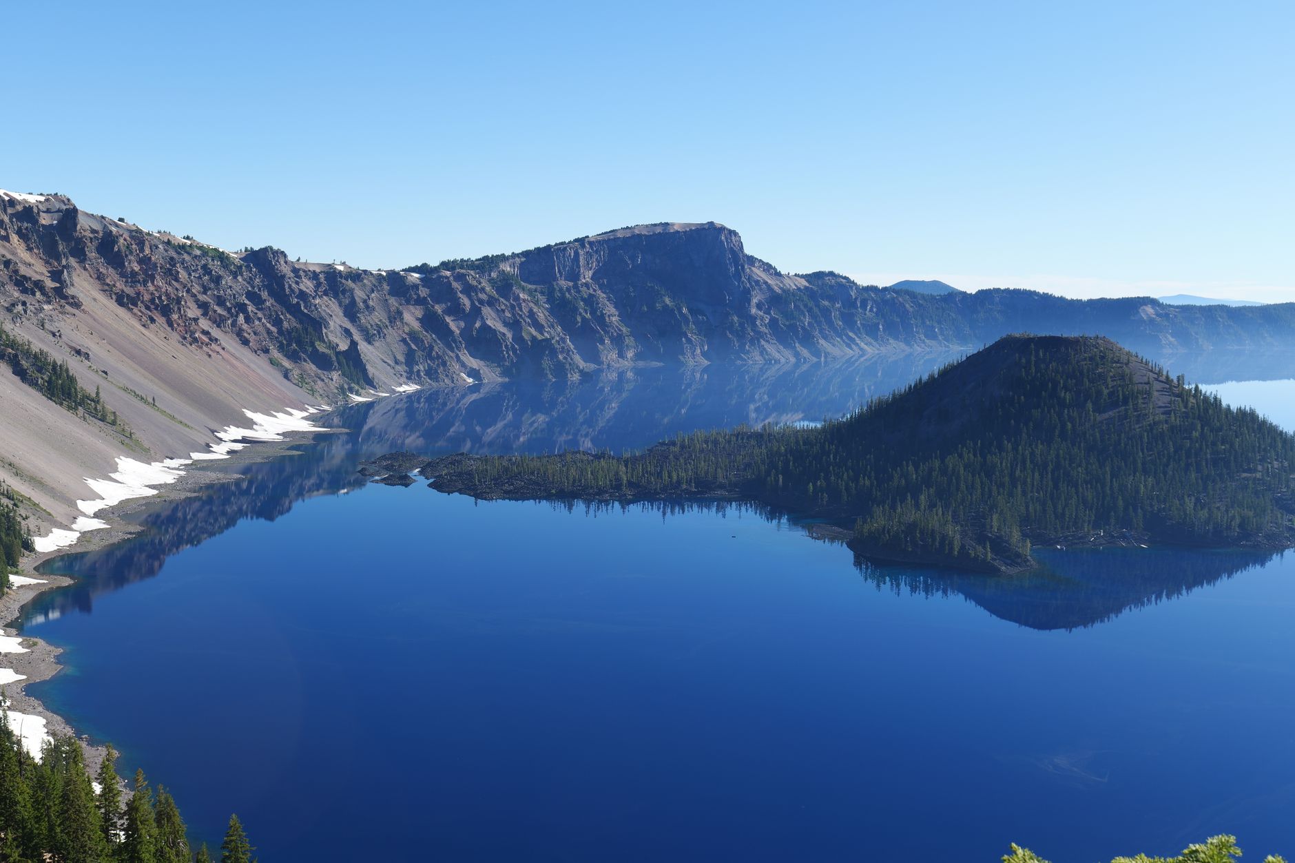 Aerial shot of Crater Lake National Park with clear blue water and surrounding cliffs.
