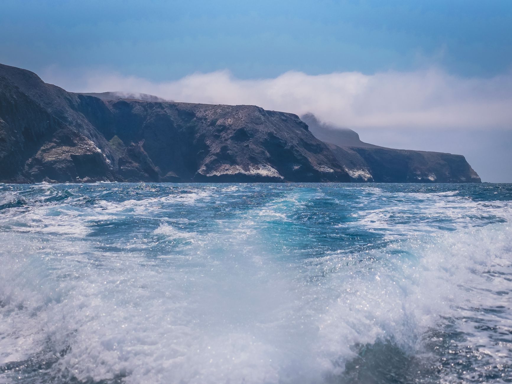 Vibrant ocean waves crash against stunning coastal cliffs under a clear blue sky.