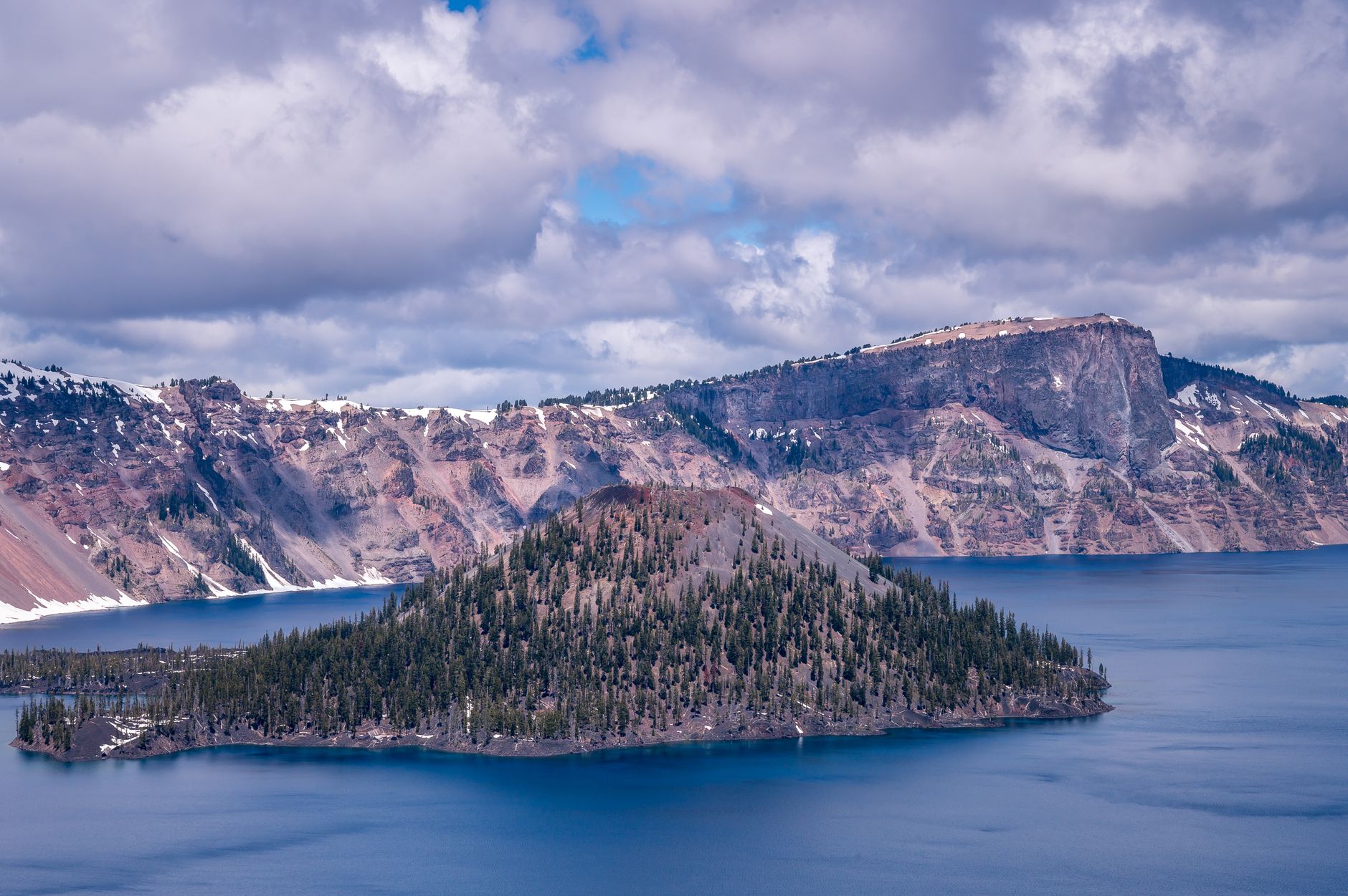 Breathtaking view of Crater Lake with rocky cliffs and blue waters under cloudy skies.
