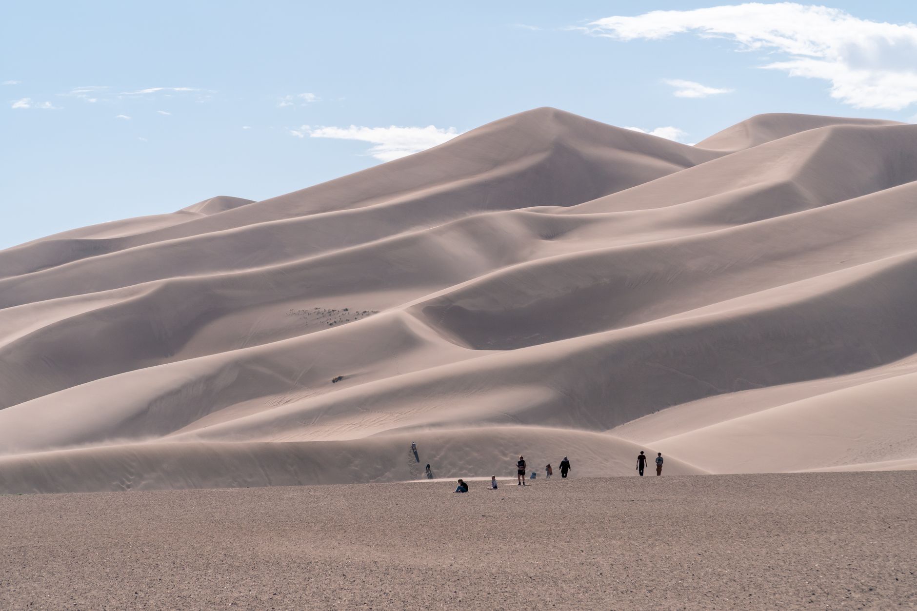 A group of people hiking the striking sand dunes in Colorado under a bright blue sky.