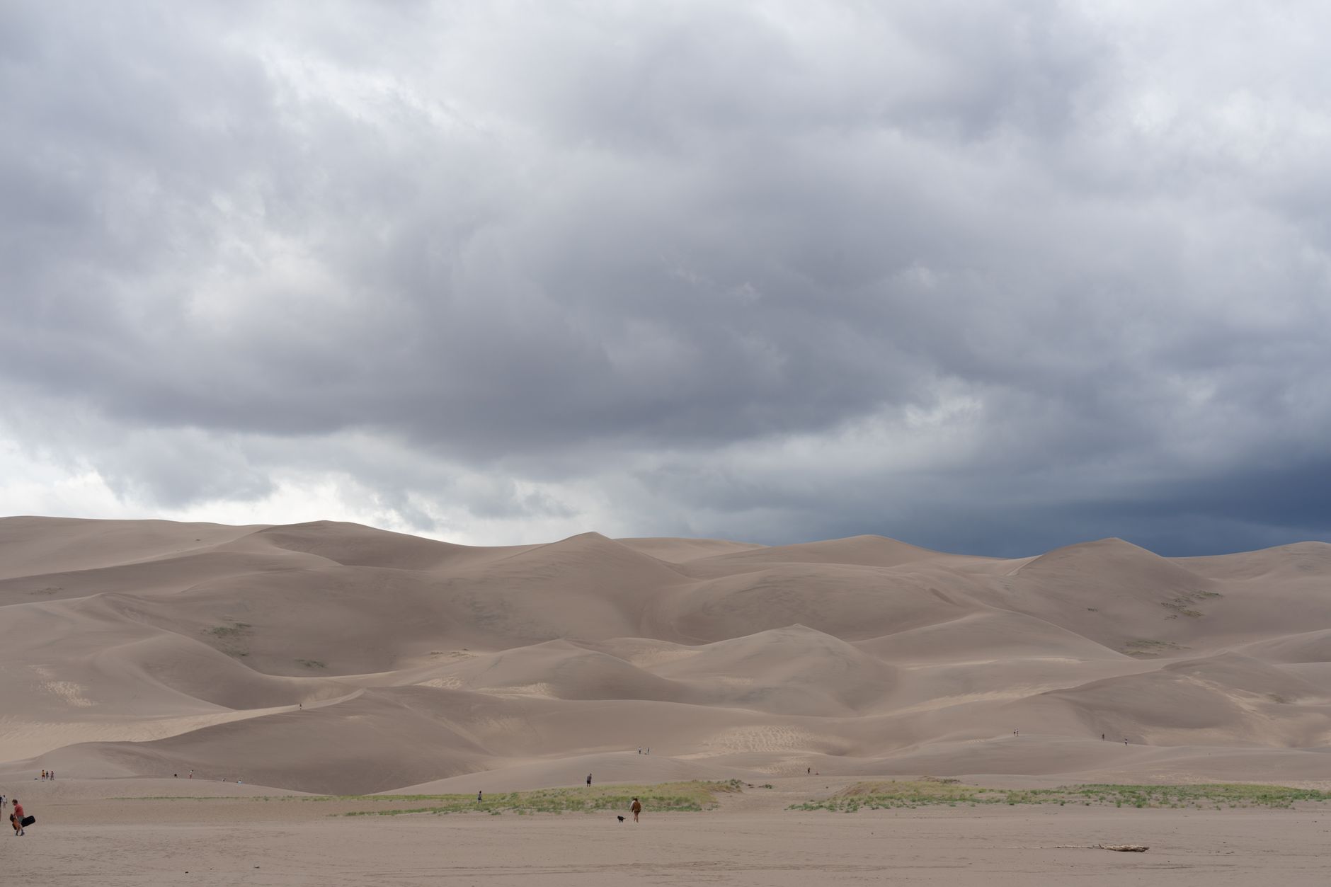 Expansive sand dunes under a dramatic cloudy sky in Great Sand Dunes National Park, Colorado.