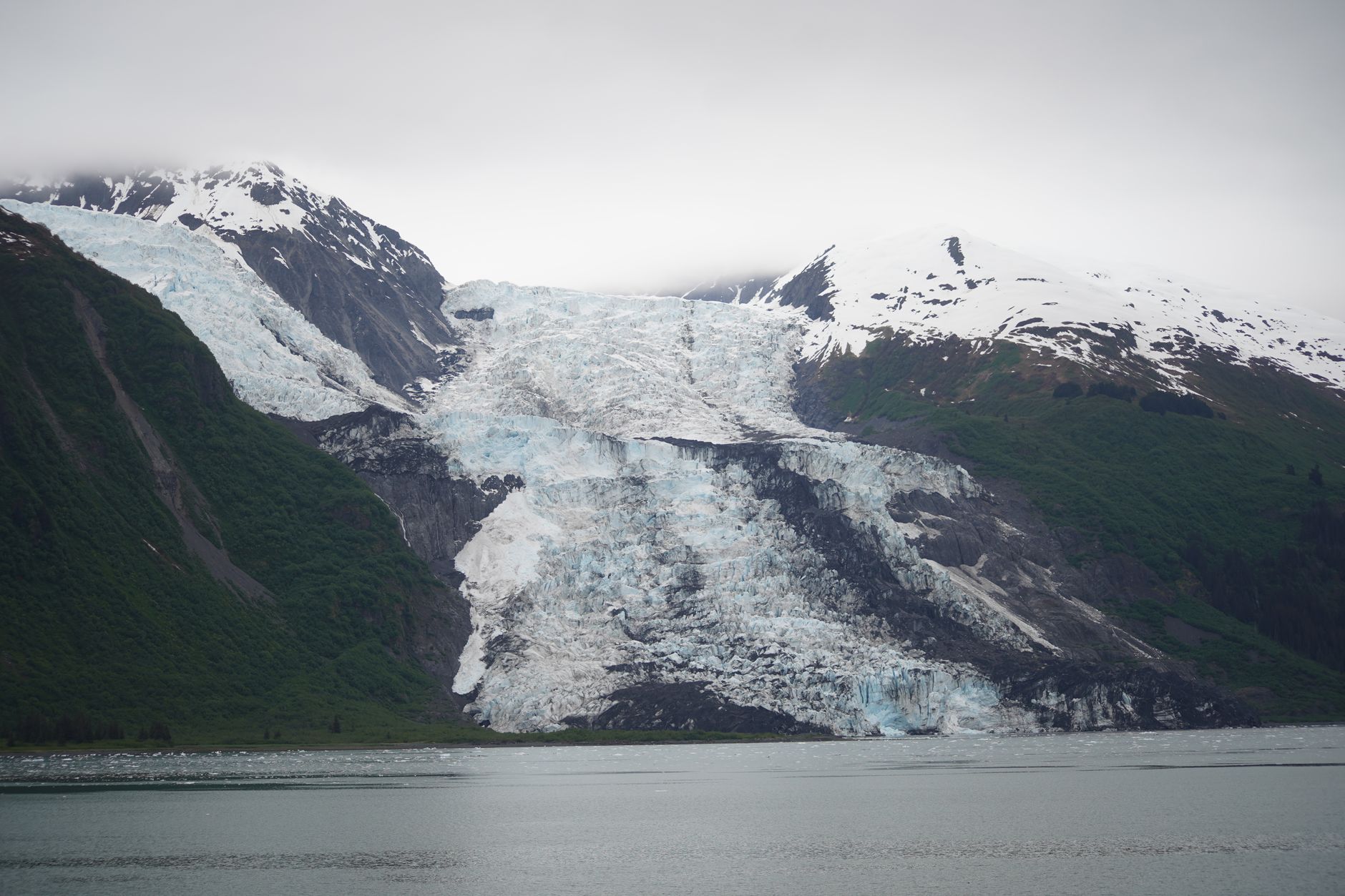 Majestic glacier flowing between snow-capped mountains by a serene lake in Alaska's pristine wilderness.