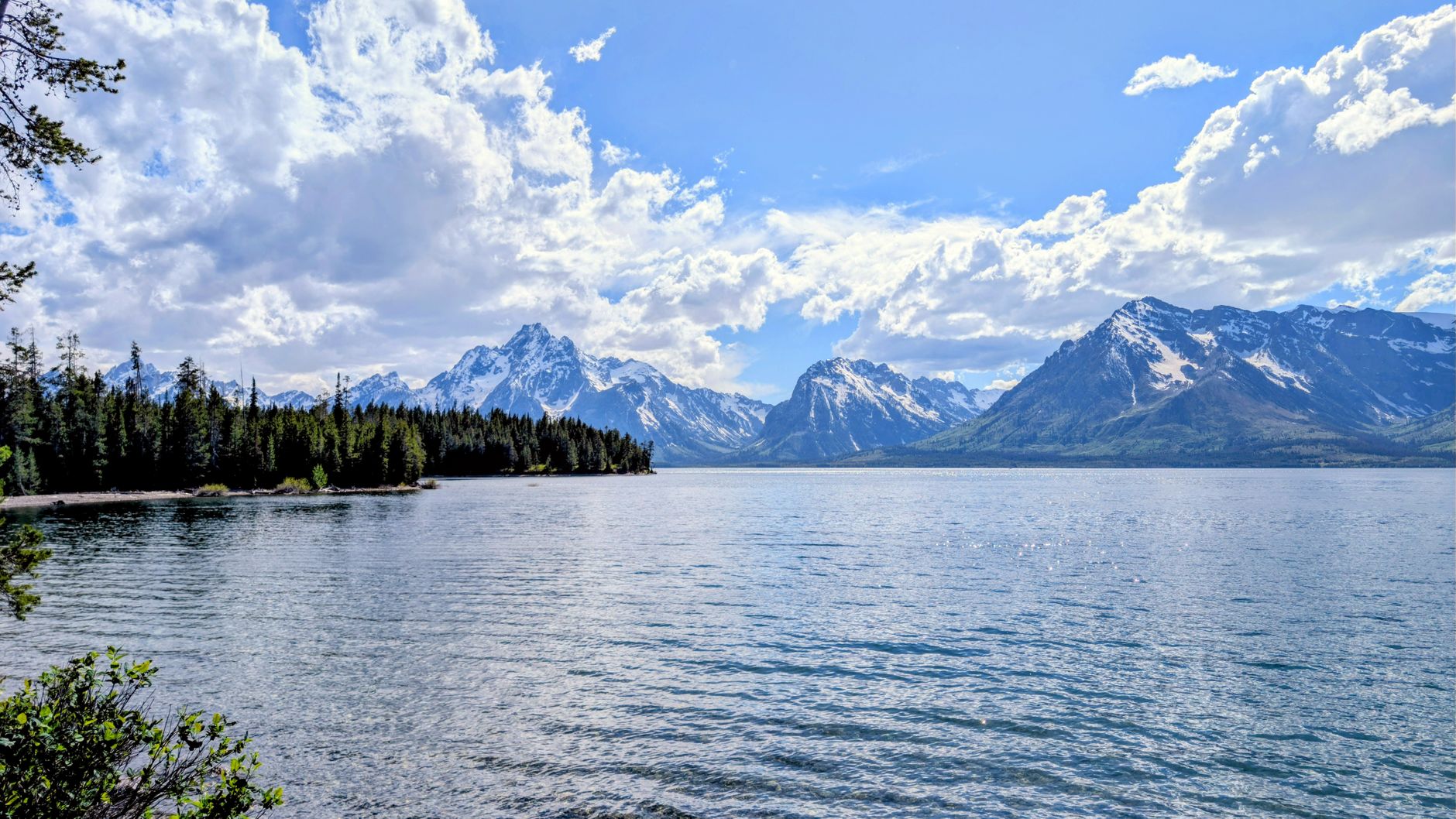 Crystal-clear Jenny Lake mirrors the majestic Grand Teton mountains under a bright sky.