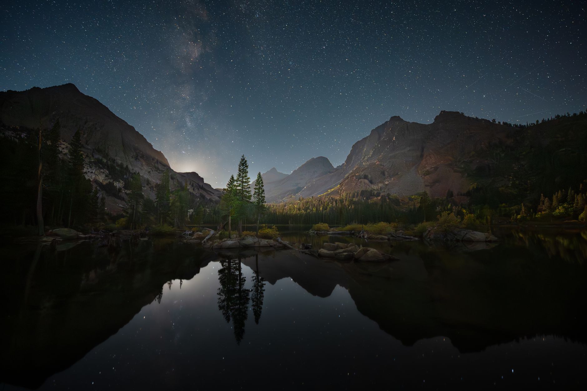 Peaceful alpine night scene with starry sky reflecting on a mountain lake in remote wilderness.