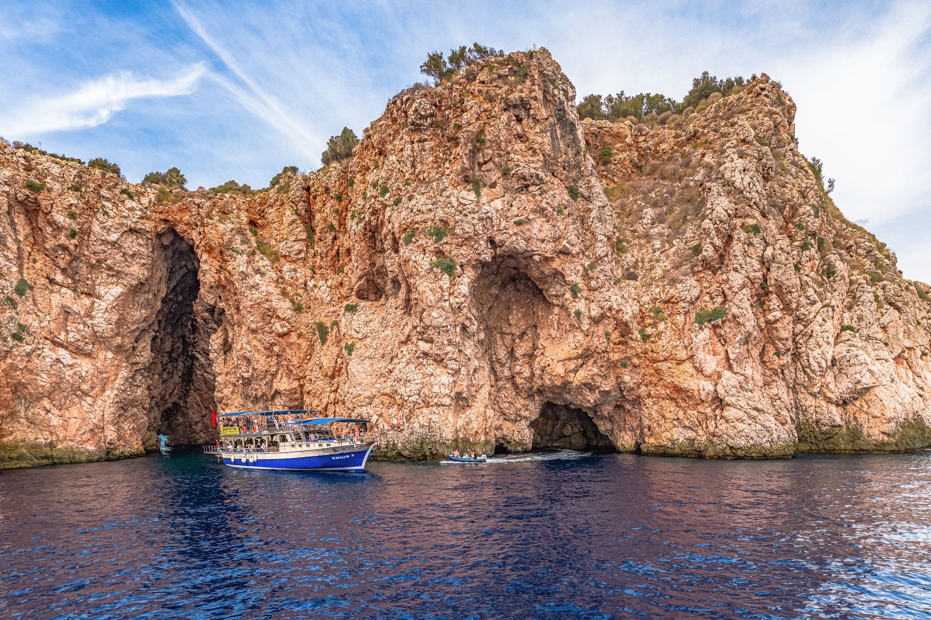 A picturesque boat navigating by rugged cliffs and sea caves in a serene coastal setting.