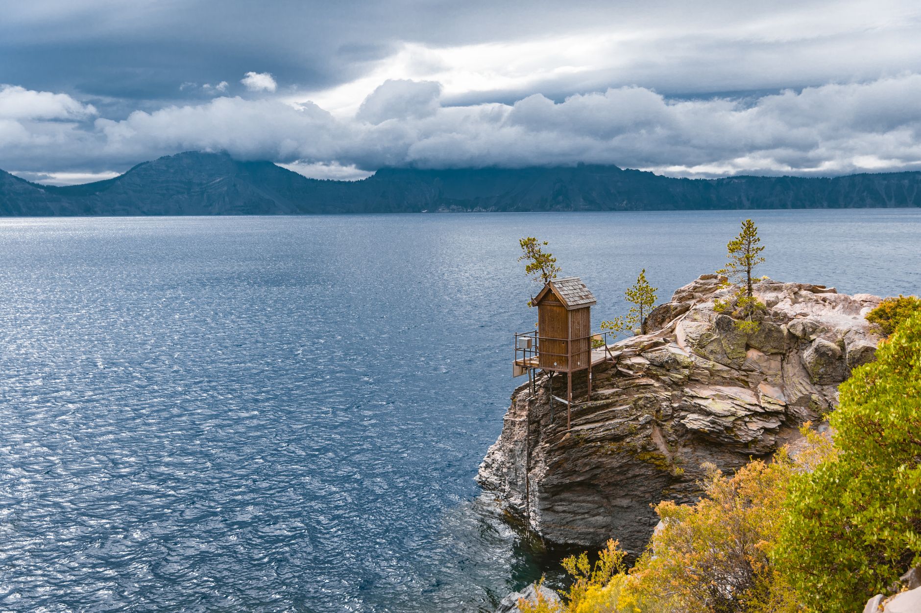 Beautiful Crater Lake view with clouds, hut on cliff, and serene water scenery.