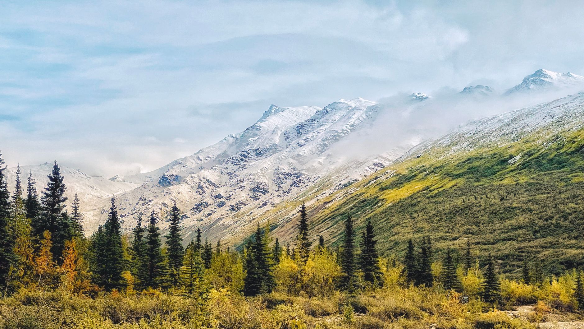 Breathtaking view of Alaskan mountains with autumn foliage and partial fog cover.