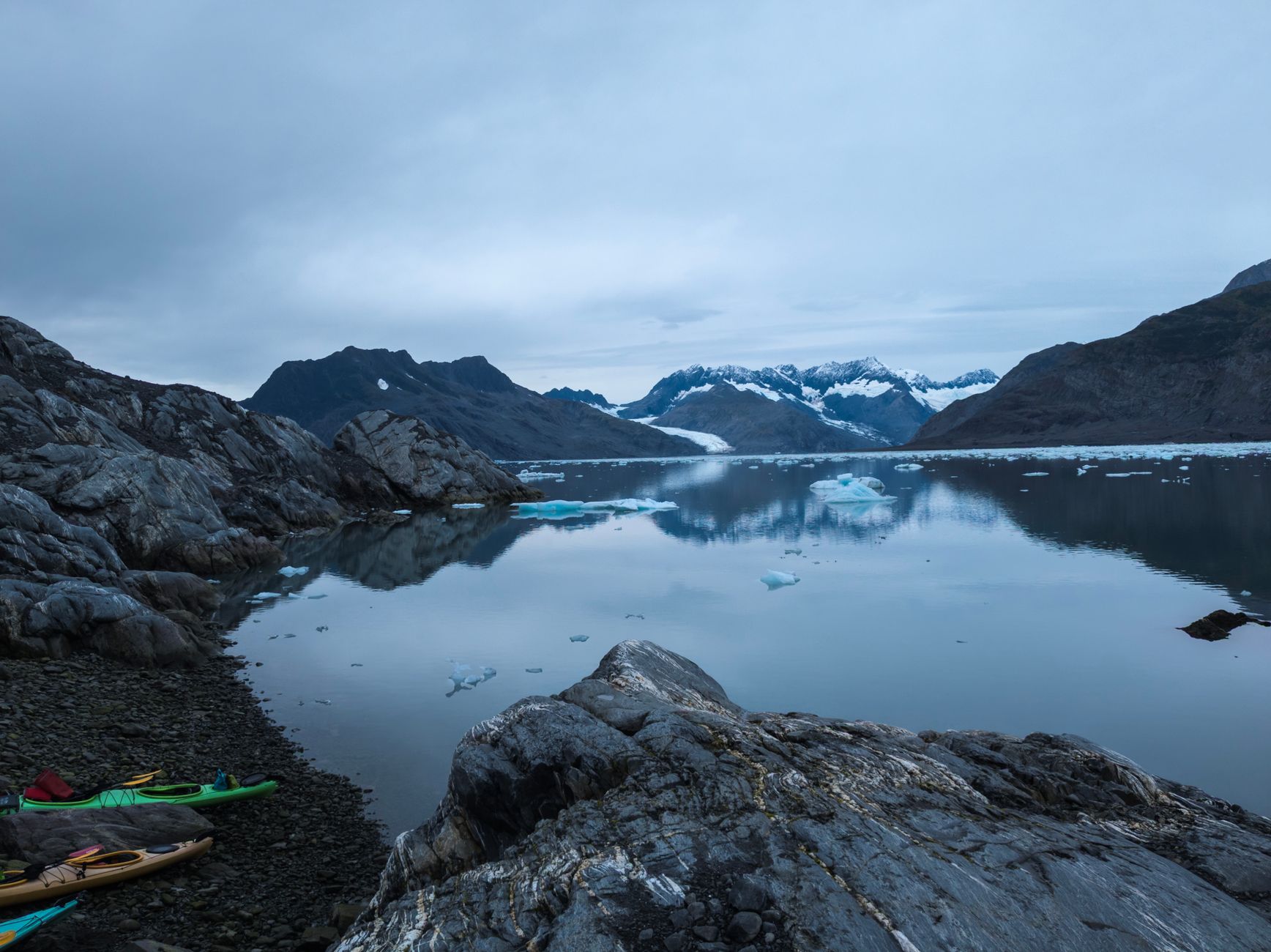 A tranquil lake reflecting majestic snow-capped mountains and kayaks on the shore.