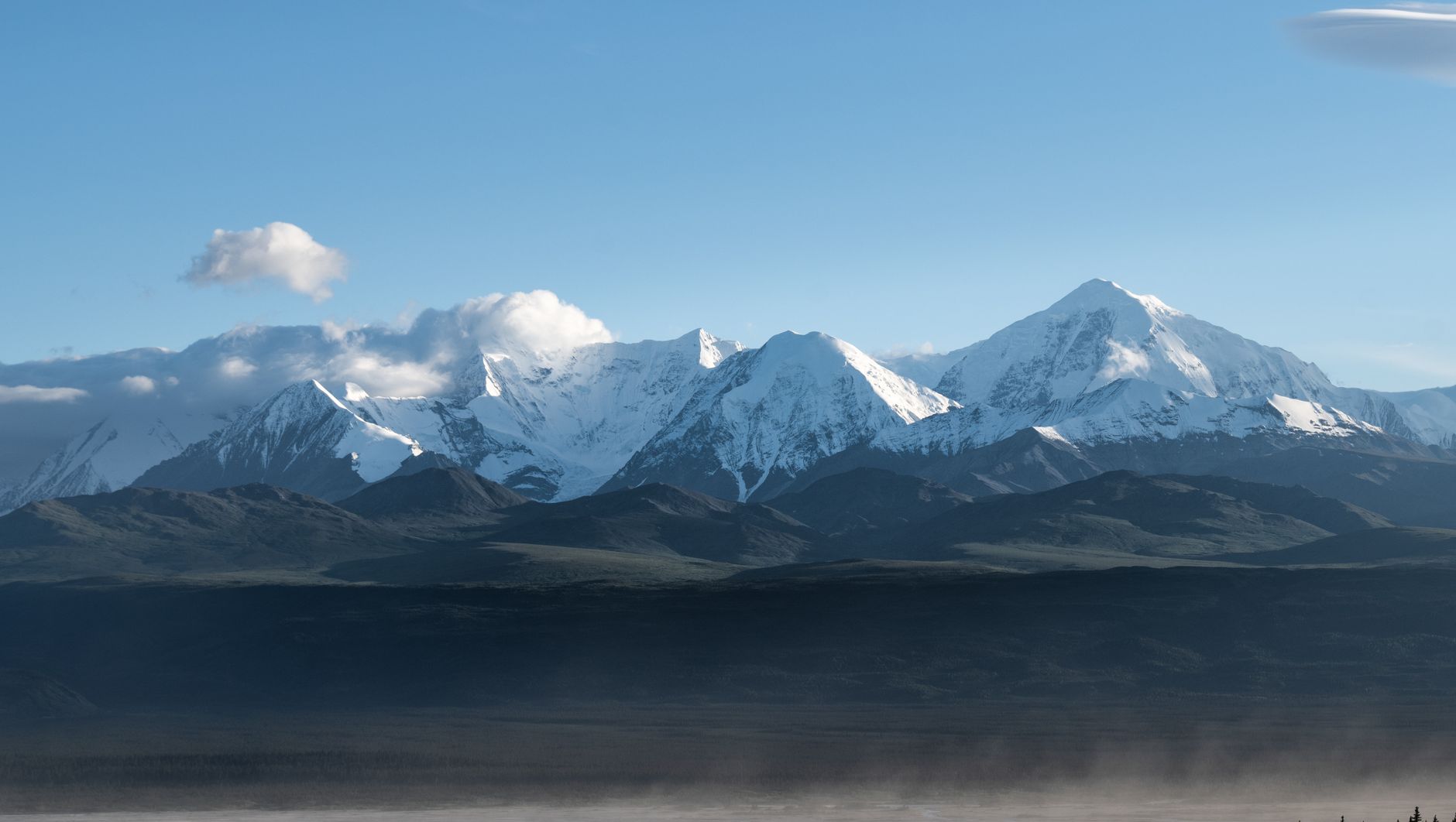 Snow-covered Denali mountains in Alaska, featuring clear blue skies and misty valleys.
