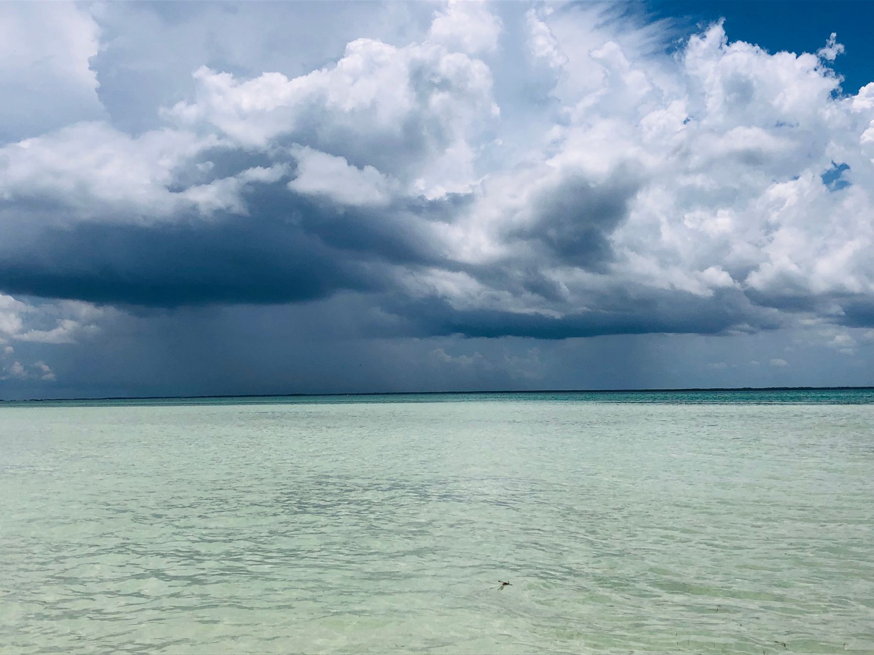Dramatic storm clouds gather over the turquoise Caribbean Sea near an island.