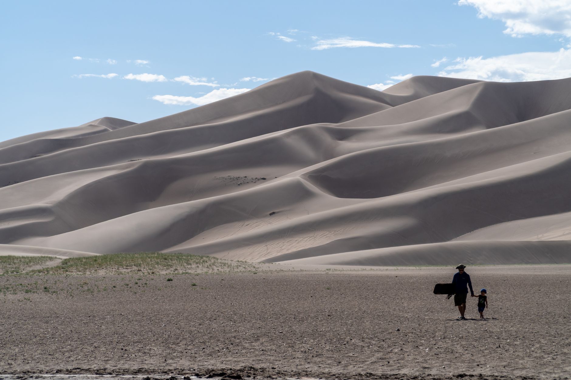 A father and son hiking together at the Great Sand Dunes in Colorado under a bright sky.