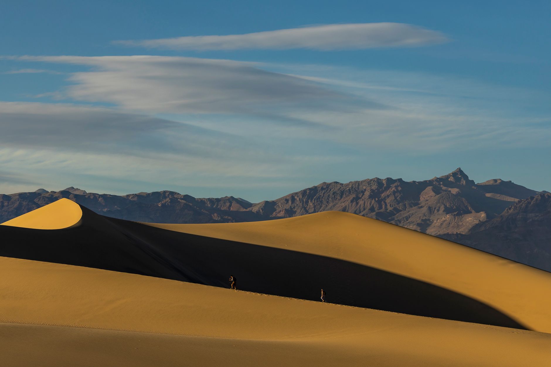 A breathtaking view of sand dunes with distant mountains under a clear sky, depicting solitude and vastness.