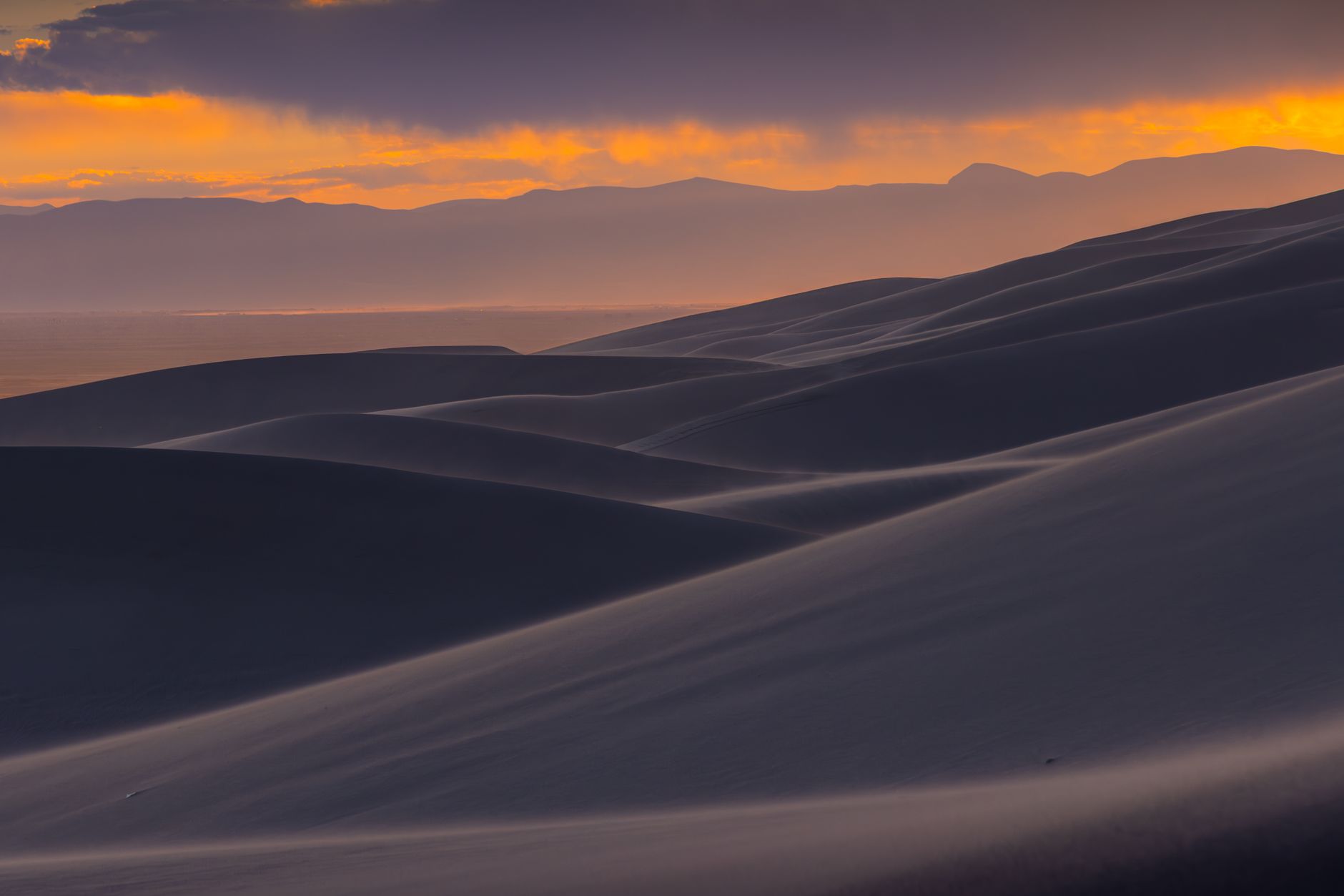 Stunning sunset view over the Great Sand Dunes with mountains in the background.