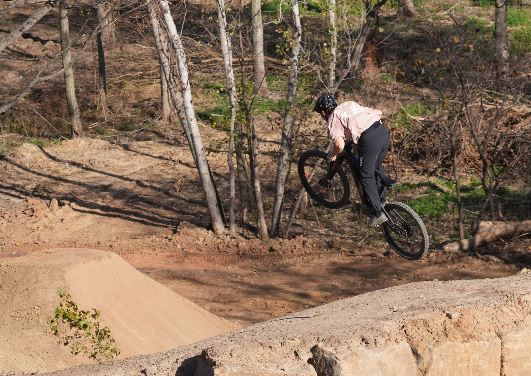 Mountain biker in mid-air jump on forest trail, showcasing skill and adrenaline of off-road cycling.