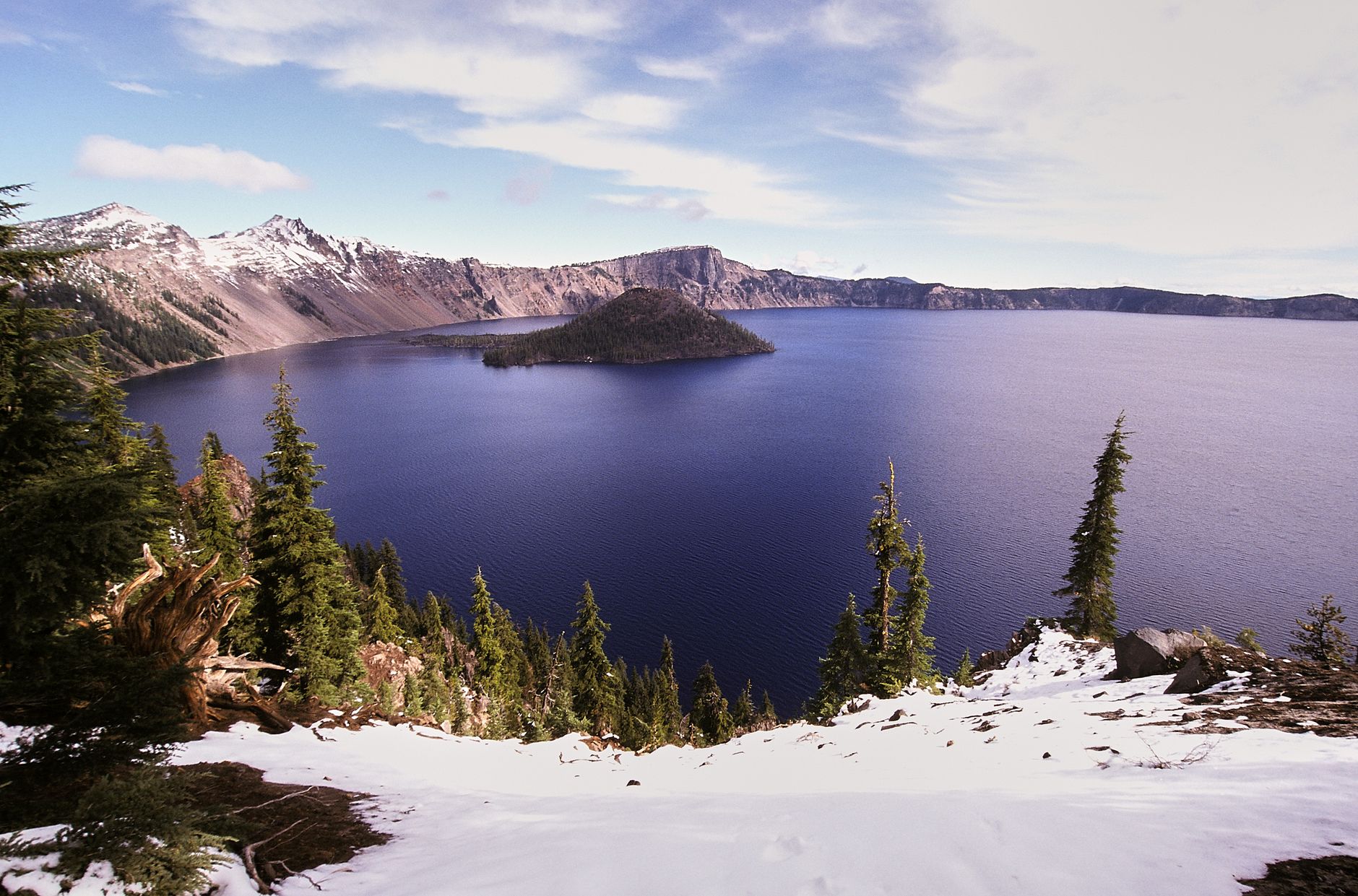 Stunning perspective of Crater Lake surrounded by snow-capped mountains in Oregon.