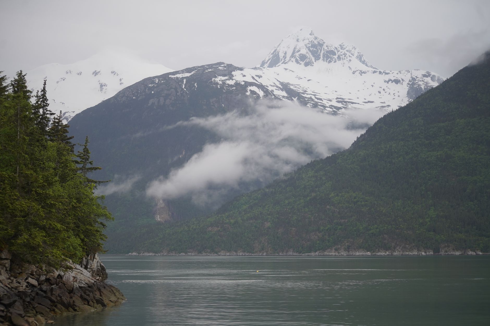 Serene landscape of Alaskan mountains, forests, and lake with drifting clouds.